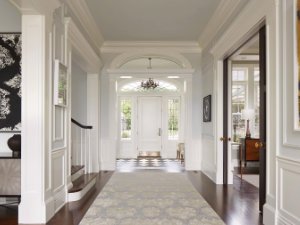 Hallway and foyer with white trim and dark wood floors looks towards the front door with a staircase to the left and double doors leading to a sitting room on the right.